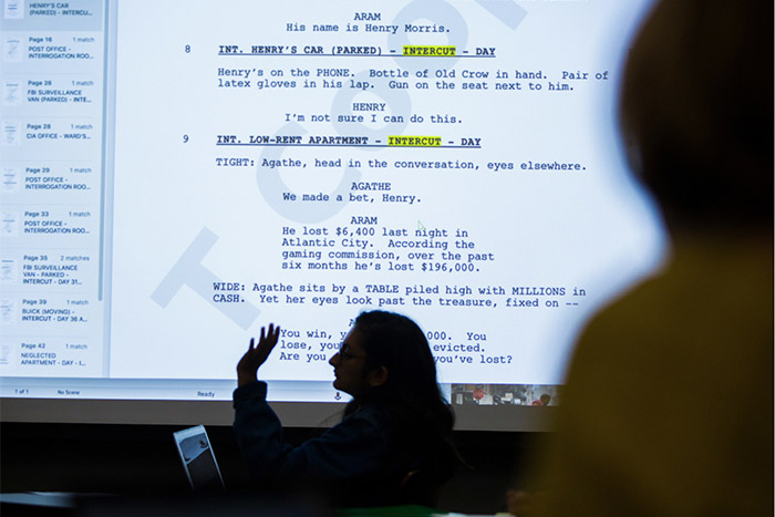 A student speaks, a script is projected on a screen behind them