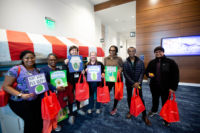 A group of employees pose with their freebies and signs with phrases about fruits and vegetables