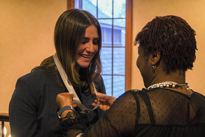 A woman puts a ribbon around another young woman's neck for the Women of Excellence Awards