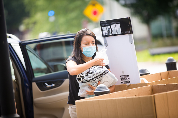 A young woman wearing a mask puts belongings in a bin for moving in