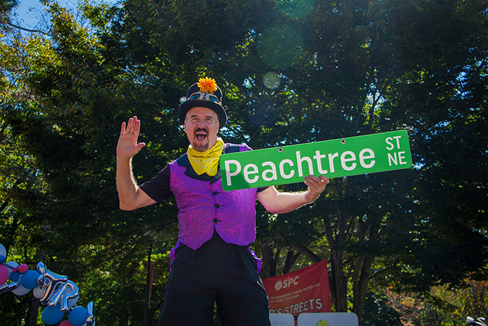 A man wearing a purple vest and hat holds a Peachtree Street sign