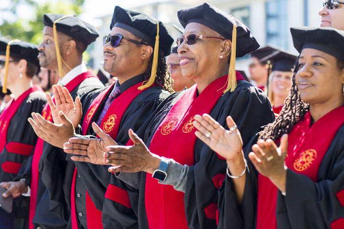 Graduates clap while wearing bright red regalia
