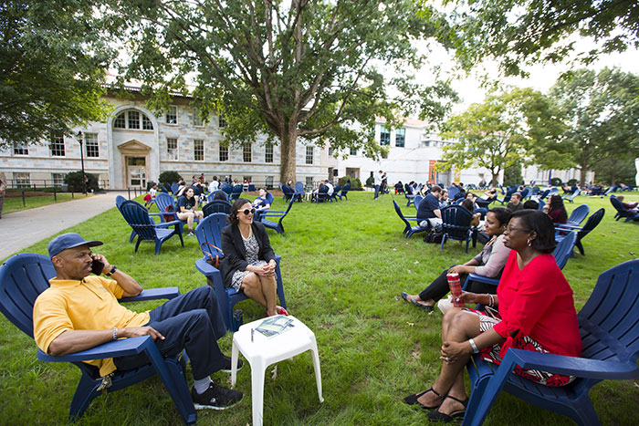 Several Emory community members speak with each other while seated in Adirondack chairs on the quadrangle
