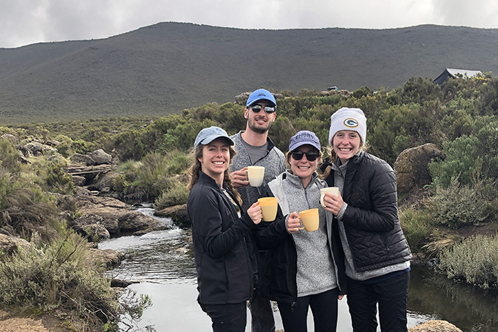 Four hikers hold coffee mugs in front of the mountain