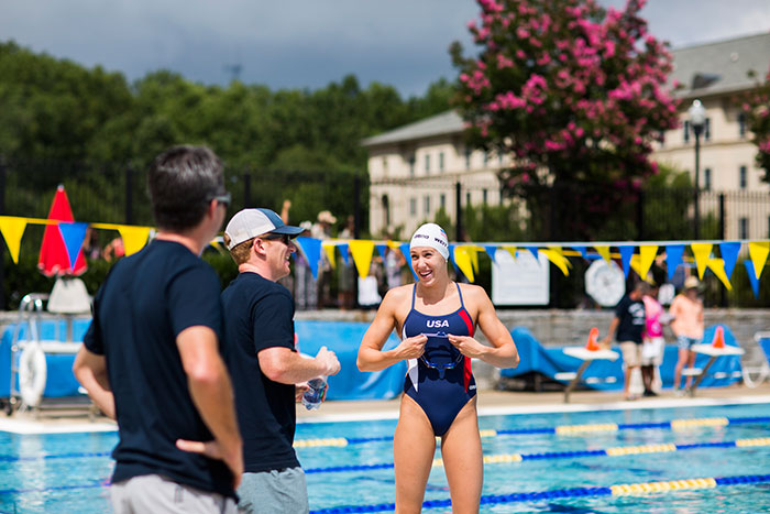 female swimmer talking to persons beside the pool