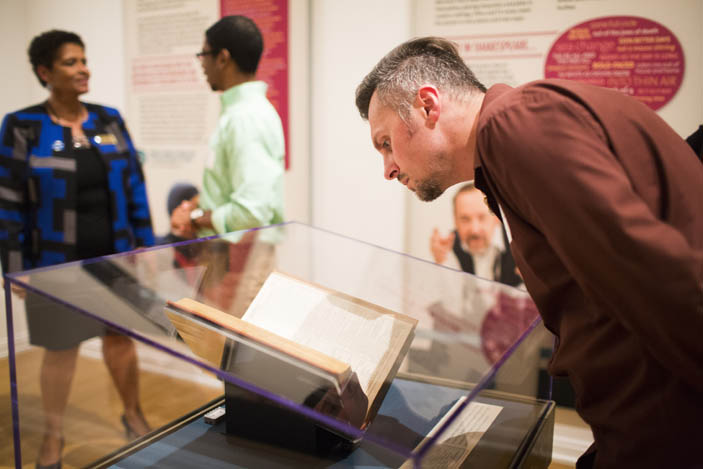 Museum visitors discuss the first folio with the folio itself in the foreground.