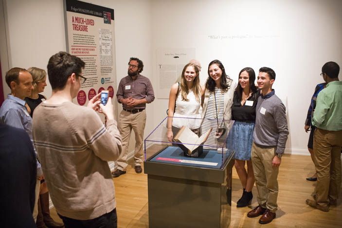 A man takes a group photo of four visitors with the First Folio