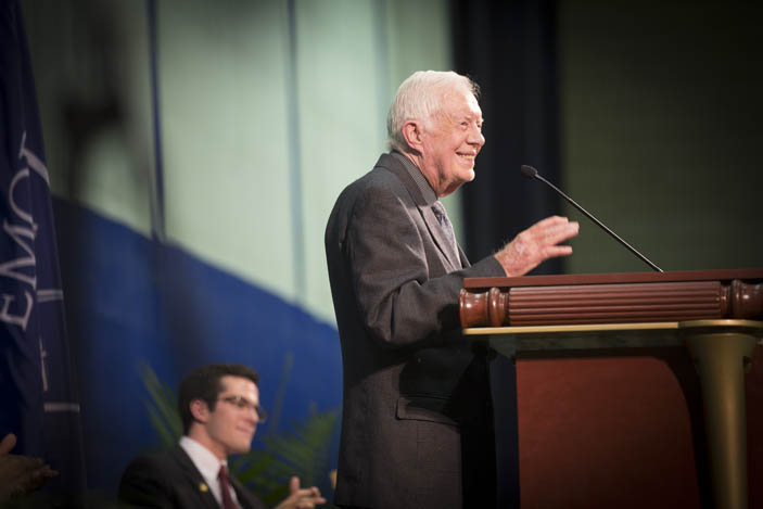 Side view of President Carter speaking at the podium, hand raised in a gesture.