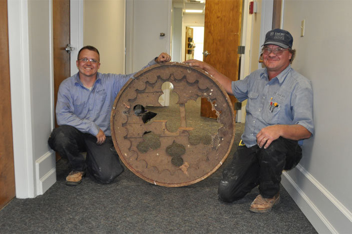 Gary Brown (left) and Al Mitchell, of Oxford's facilities management team, are seen holding a handmade, decorative cover that fit the gable vent on the building's north side. Using photographs to confirm that it was used in the building, the cover was restored, and it is now back in its original place.