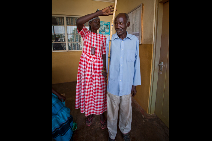 Asio Adaladiza, health center supervisor (on left) demonstrates how to measure a patient for the correct dose of Mectizan with Chandia Grace, a community drug distributor in Uganda's Moyo district.