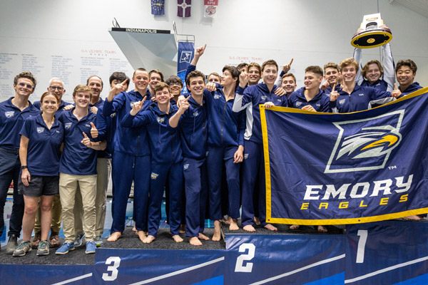 Group photo of the Emory women's swim and dive team holding up a team banner with the Emory Athletics Eagle logo