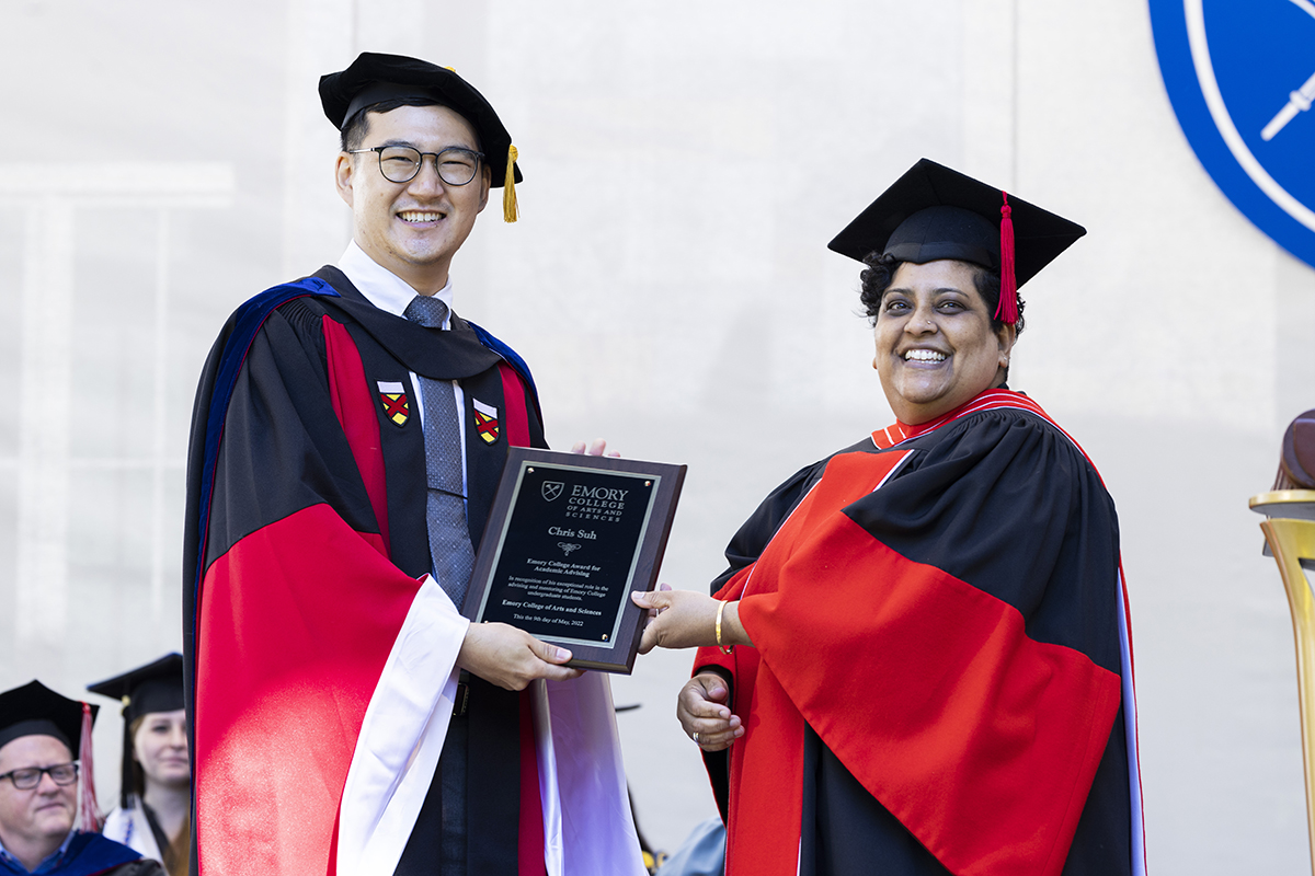 Chris Suh receives an award from Deboleena Roy. Both are wearing academic gowns.