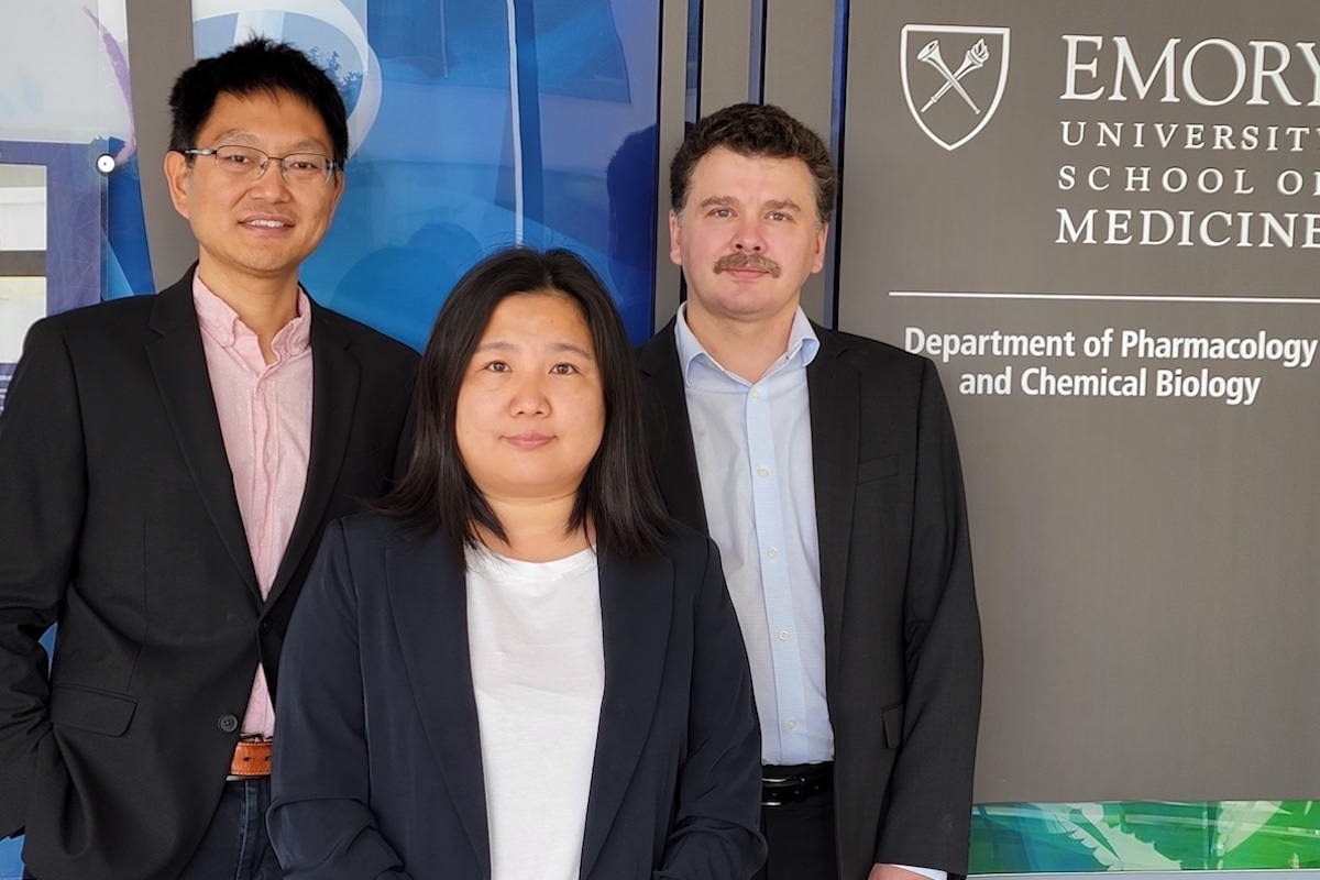 Three co-first authors stand in front of the Emory School of Medicine Department of Pharmacology and Chemical Biology sign