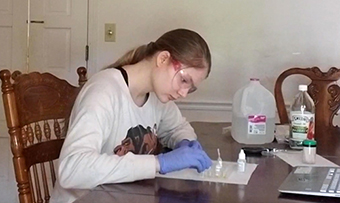 A student works at home on a lab assignment wearing PPE
